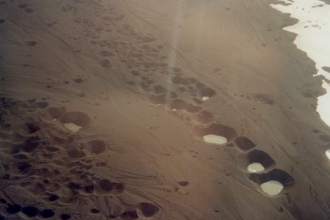 Pools of water in holes in brown ground seen from above