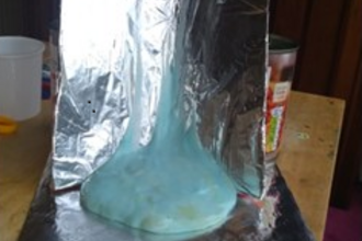 Upright tinfoil sheet with pale blue paste sliding down it and pooling at the bottom