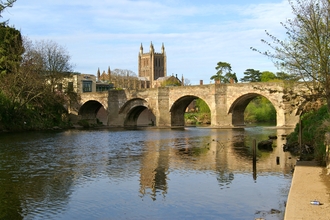 View of wide river flowing under 4 arches of a stone bridge with cathedral tower behind