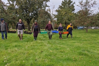 Six people walking in a grassy field with coloured trays of fruit carried between them