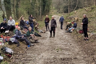 Group of around 15 people stood and sat alongside a track through a wood in winter