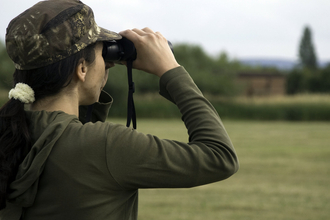 Woman with a pony tail looking away through binoculars wearing a camouflage print cap