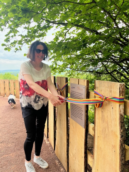 Woman cutting a multi-coloured ribbon tied across wooden fencing beneath tree