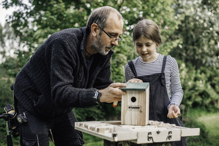 Man and little girl inspecting a bird box
