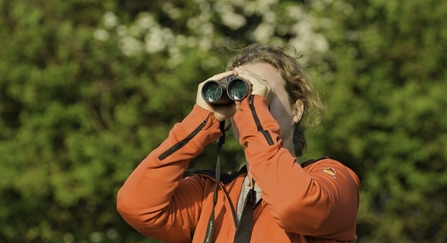 Woman in orange top looking through binoculars