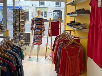 View through a shop with rails of clothes each side and back of mannequin in window display