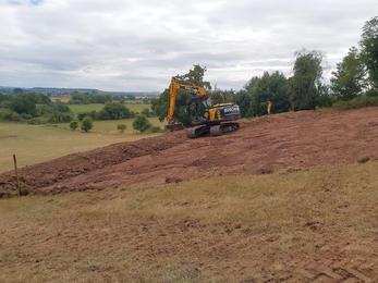 Small yellow digger moving earth on sloping field