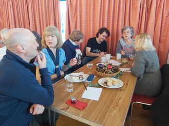 Six people sat around a table with cakes and other food