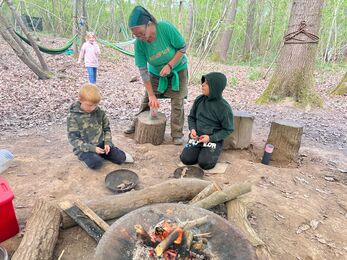 Two boys and a woman beside a fire bowl in the woods