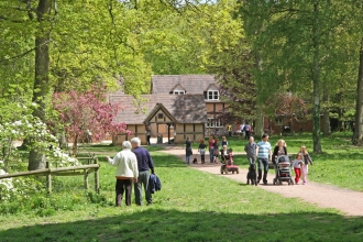 Families walking on tree-lined path with timber-framed buildings in background