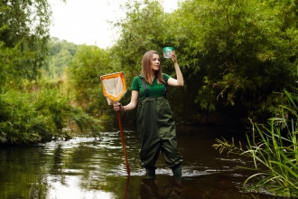 Girl standing in river in waders with net and jar