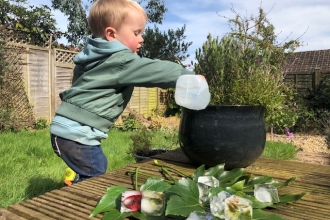 Young boy pouring water with ice cubes and leaves in foreground