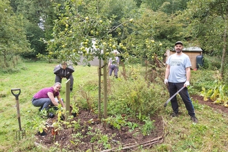 A group of three adults tending to a a garden bed with an apple tree growing in the centre