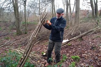 Man stood in woodland in winter tying together a bundle of poles