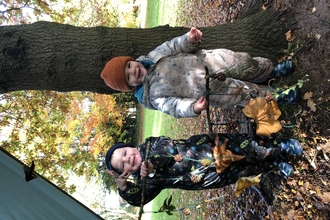 Two toddlers holding twig and leaf crafts, smiling.