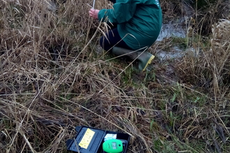 Girls in green coat crouching in long vegetation, turning to smile at camera