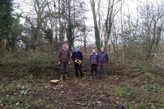 Four people stood in a woodland clearing facing the camera, winter