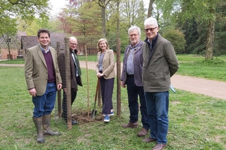 Four adults stood around a newly planted tree on an area of grass