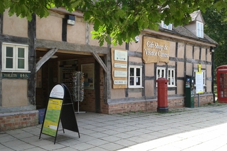 Slanted view of a timbered building with central open archway and A frame, post box and phone box visible in front