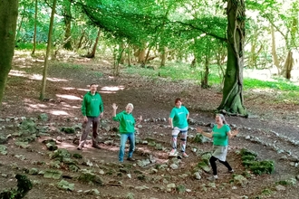 Four people in green T-shirts stood in a wood in circles of small stones