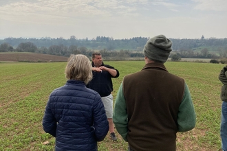 The backs of a man and woman facing a man who is talking in an arable landscape