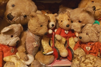 A group od teddy bears on a shelf, several wearing red jumpers