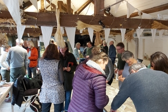 People stood in small groups in low-beamed room decked with white bunting