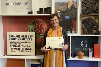 Woman holding a certificate in front of wall of images and shelves