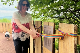 Woman cutting a multi-coloured ribbon tied across wooden fencing beneath tree