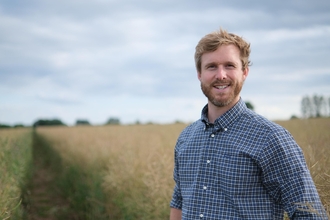 Man with blond hair wearing checked shirt smiling at camera; arable field in background