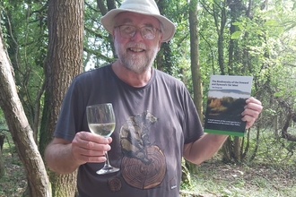 Man holding book in one hand and wine glass in the other, smiling at camera
