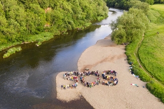 Letters SOS spelt out by people stood on riverside beach