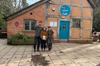 Three people stood outside a timber-framed building