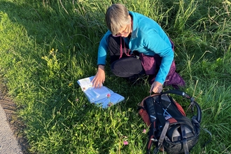 Woman knelt down in grass with open book and rucksack