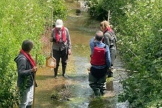 Four people wearing life jackets and holding nets stood in stream