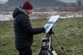 Man stood outdoor in winter painting on easel with flooded field and trees in background
