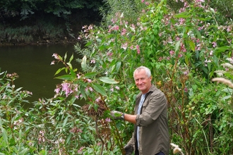 Man stood beside huge plant with pink flowers, a river visible in background