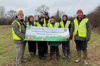 Group of seven people in outdoor clothes and hi-vis vests holding a banner