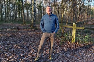 Man standing in woodland in winter with a blue top and brown trousers