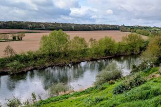 View of tree-lined stretch of river with ploughed field on far bank