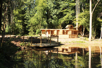 View across woodland pond with wooden building 