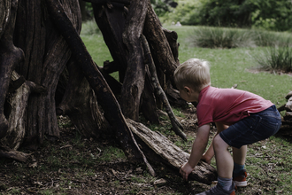 Young boy in red tee shirt lifting a log to add to a den