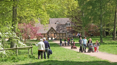 Families walking on tree-lined path with timber-framed buildings in background