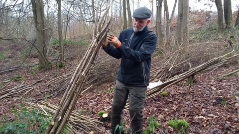 Man stood in woodland in winter tying together a bundle of poles