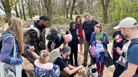 A group of people surrounding their walk leader looking at a woodland plant that he is showing them