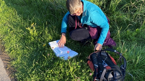 Woman knelt down in grass with open book and rucksack