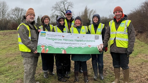 Group of seven people in outdoor clothes and hi-vis vests holding a banner