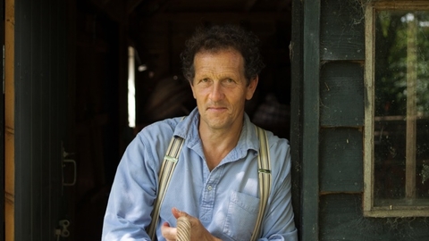 Man with dark hair wearing a blue shirt and braces leant in a doorway