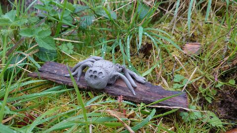 y clay spider sitting on some bark surrounded by green moss and grass
