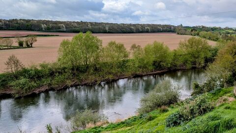 View of tree-lined stretch of river with ploughed field on far bank